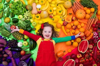 little girl surrounded by healthy fruit and vegetables
