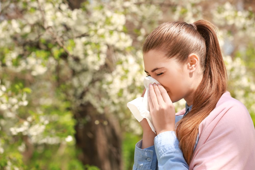 sneezing girl with tissue among blooming trees